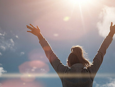 Glückliche Frau hebt die Hände zur Sonne