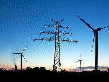 Strommast einer Hochspannungsleitung und Windräder in der Abenddämmerung bei Brunsbüttel in Schleswig-Holstein.