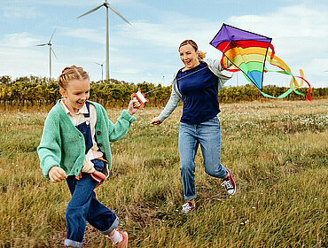 Mutter und Kind beim Drachensteigen mit Windräder im Hintergrund